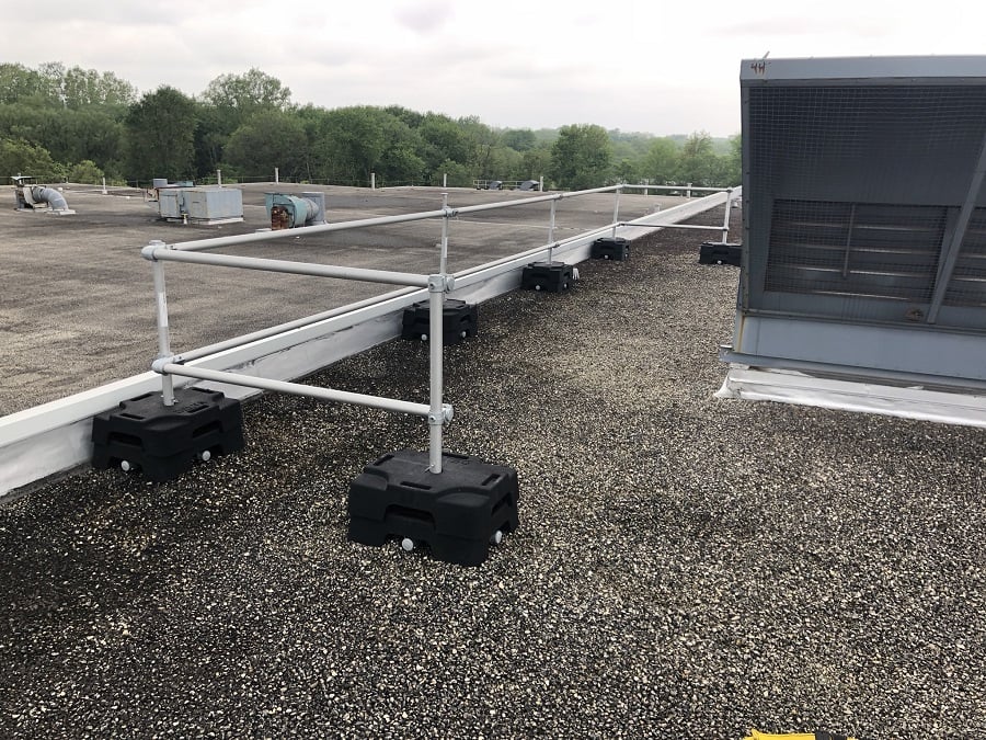Freestanding guardrail installed on a roof with parapet. VSS Compact configuration with rubber counterweight and aluminum tubing to protect HVAC component